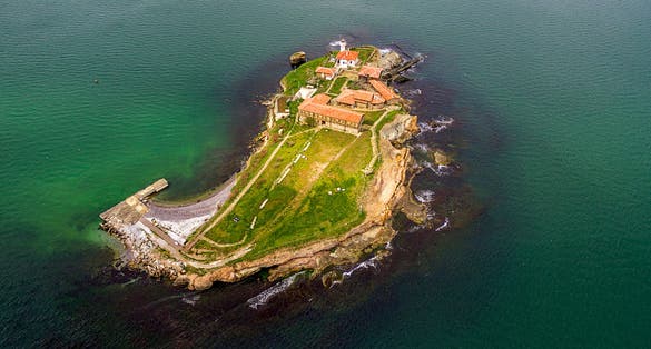 photo of view of Saint Anastasia Island in Burgas bay, Black Sea, Bulgaria. Lighthouse tower and old wooden buildings on rocky coast,Burgas Bulgaria.