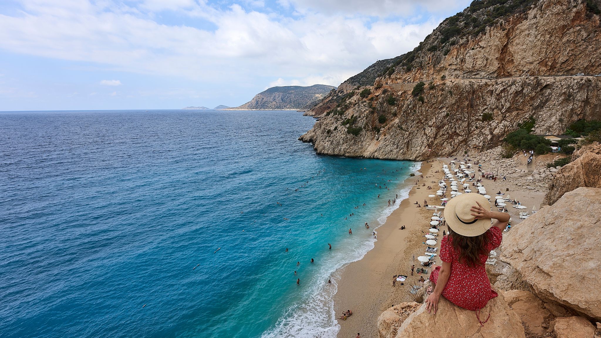 Girl in red dress and hat posing and watching panorama landscape of Kaputas Beach (aka Kaputaş Plajı) of Mediterrane.