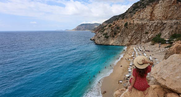 Girl in red dress and hat posing and watching panorama landscape of Kaputas Beach (aka Kaputaş Plajı) of Mediterrane.