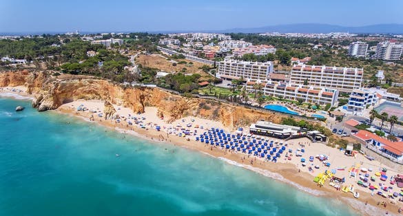 Aerial drone shot of a busy beach, amazing cliffs, vegetation and also buidlings in the background. Praia do Vau, Portimao, Portugal.