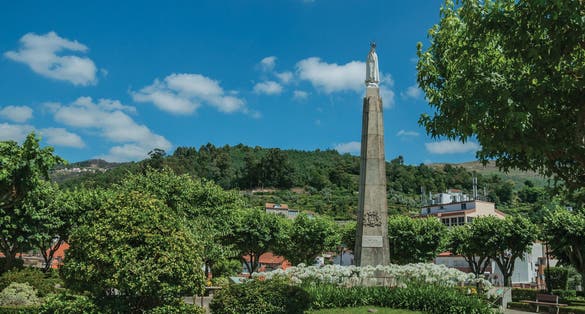 Marble statue of Our Lady on stone pillory at flowered garden, in a sunny day at Seia. On foothill mountains, this friendly town in eastern Portugal is also known for its delicious artisanal cheese.