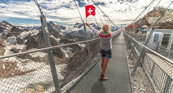 photo of woman with Swiss flag on Titlis cliff walk suspension bridge. Top of Titlis mountain with glacier in the Uri Alps in Switzerland, Europe. Summer season.