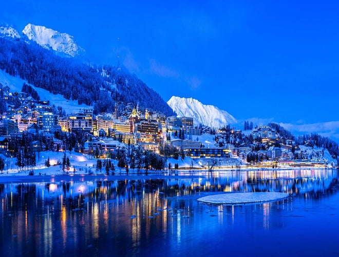 St. Moritz at dusk with snowy mountains, festive lights, and reflections on the frozen lake..jpg