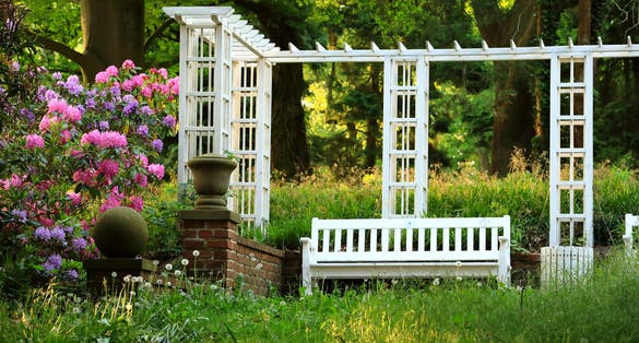 photo of view of Scenery in a Park in spring: a white pergola, bench an flowering Rhododendrons on the left (Knoops Park , Bremen, Germany.