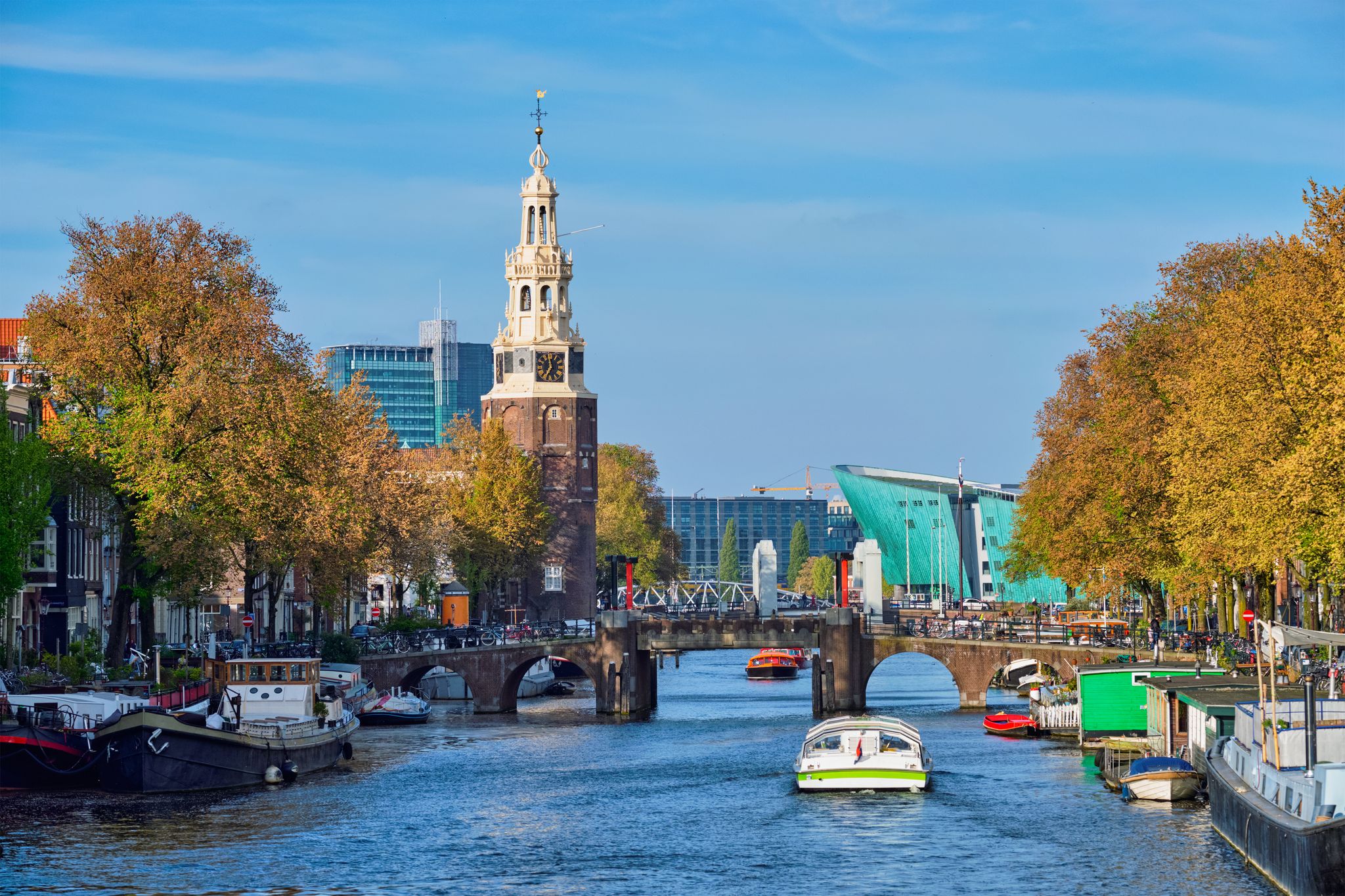 Photo of Amsterdam cityscape with canal boats and medieval houses and NEMO Science museum and Montelbaanstoren Tower, Netherlands.