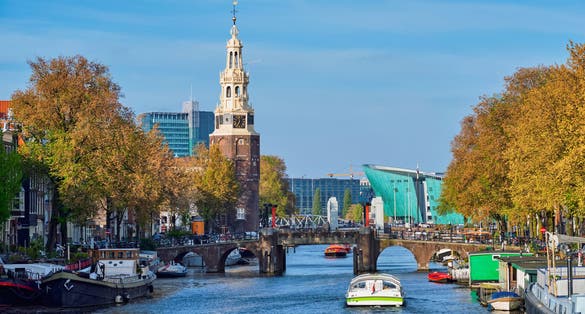 Photo of Amsterdam cityscape with canal boats and medieval houses and NEMO Science museum and Montelbaanstoren Tower, Netherlands.