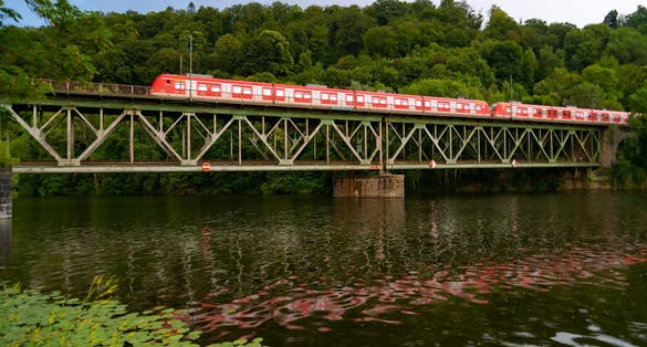 photo  of view of  Historic green railway bridge spanning over Ruhr river in Essen-Kettwig Germany. Red multiple unit train from Düsseldorf to Essen passing steel construction with reflection on a rainy summer evening.