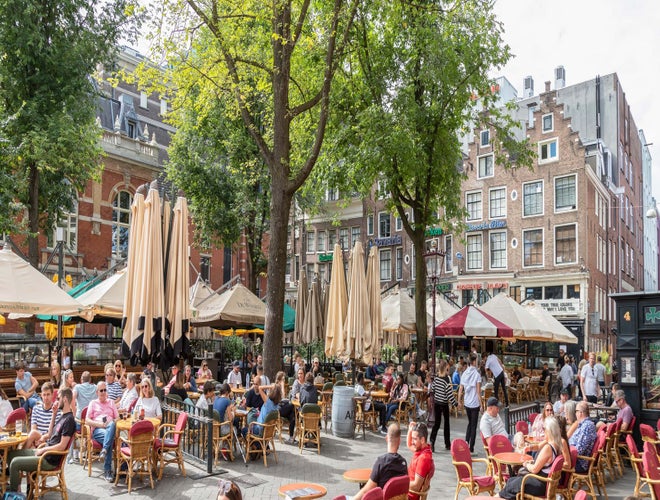 People dining and socializing at outdoor cafés in a lively Amsterdam square in summer..jpg
