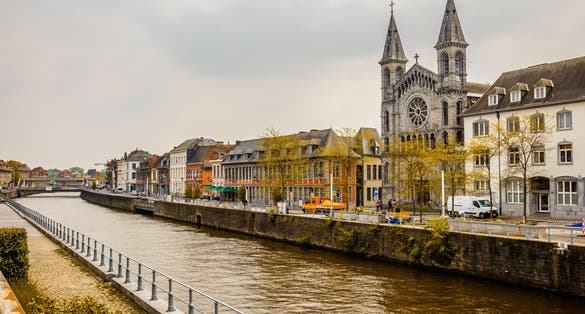 Photo of Escaut river and street with old belgian houses and facade of church of the Redemptorists of Tournai, Walloon municipality, Belgium.