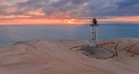 Photo of the breathtaking beauty of Rubjerg Knude Lighthouse in a mesmerizing sunset, Denmark.