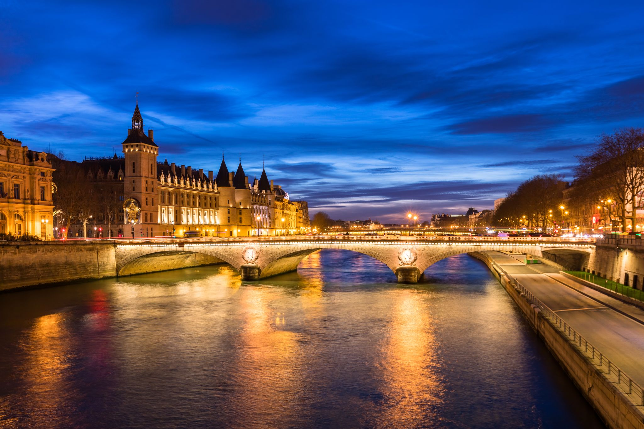 Paris city center by night with embankments of river Seine and illuminated street and historical Parisian building of Conciergerie on City island, blue hour, France.