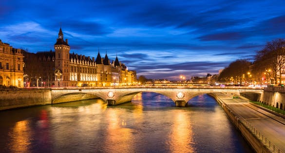 Paris city center by night with embankments of river Seine and illuminated street and historical Parisian building of Conciergerie on City island, blue hour, France.