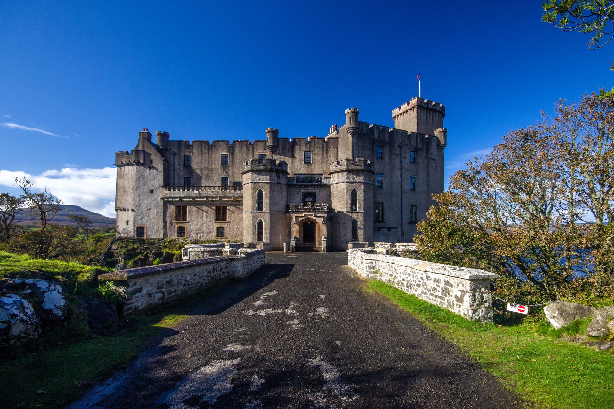 Photo of Horizontal wide angle view of beautiful Scottish Castle, bridge entrance, Dunvegan Castle Isle of Skye, Scotland. Sunny day with bright blue sky. 