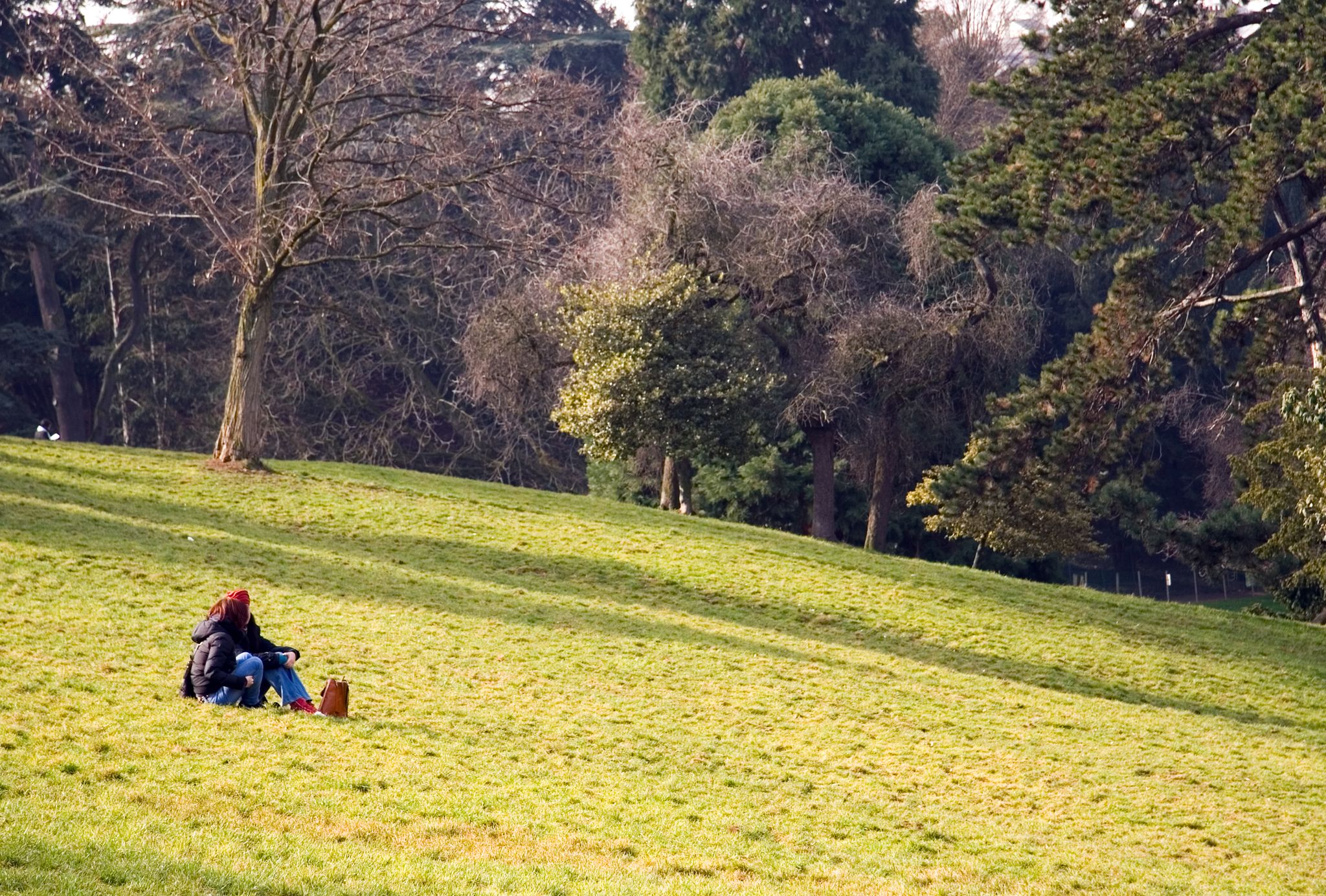 photo of two girls sitting on the ground in the Parisian Park Buttes-Chaumont on spring day in France.