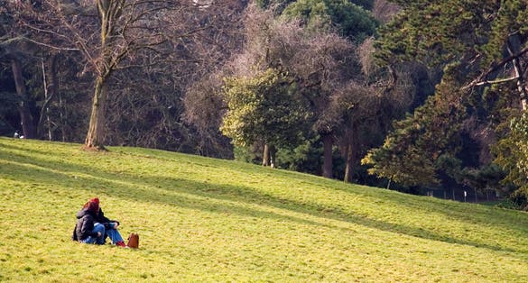 photo of two girls sitting on the ground in the Parisian Park Buttes-Chaumont on spring day in France.