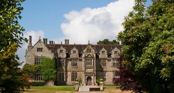 Photo of typically large English landscape garden with hedges, fences, plant and flower beds, lawn, pond and garden furniture, Chichester, England.