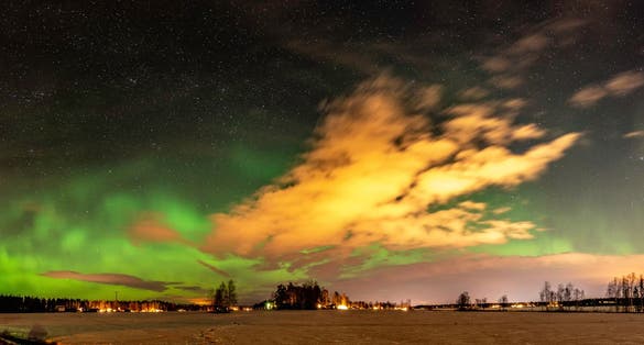 Panorama of green lights Aurora and stars shine over abandoned shed standing alone in the field, Umea city, Sweden.