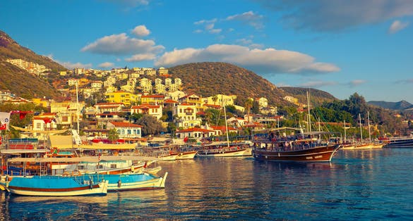 Tourist yacht sails from Kaş marina for an evening walk at sunset golden hour.