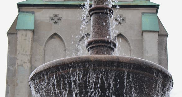 The cathedral or Domkirken in Kristiansand, Norway, Europe. In front of the church a water fountain with a pigeon sitting on its top.