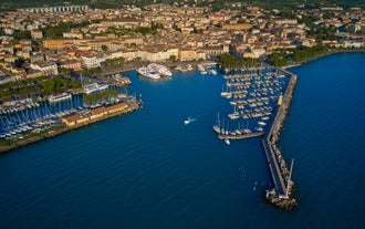 Photo of Old harbour Porto Vecchio with motor boats on turquoise water, green trees and traditional buildings in historical centre of Desenzano del Garda town, Northern Italy.