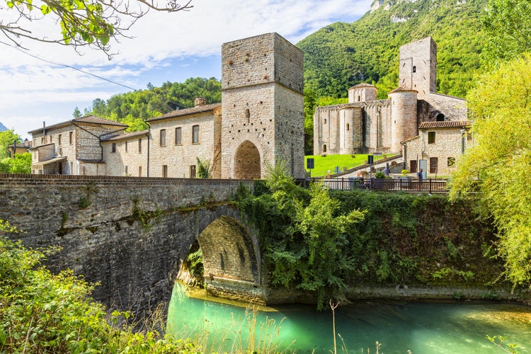 Photo of San Vittore alle Chiuse. Roman Catholic abbey and church. The edifice is known from the year 1011. Ponte Romano. Roman bridge over a small river. Italy. Marche. Ancona. 