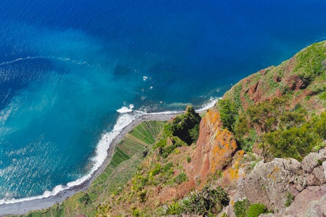 View down from the 'Miradouro do Cabo Girão' viewpoint, Câmara de Lobos. Blue Atlantic ocean and rocky coast with green agricultural fields. Beautiful volcanic landscape of Madeira island, Portugal.