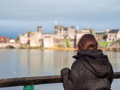 photo of Young teenager girl looking at stunning King John's stone castle with tall walls and towers. Limerick city, Ireland. Travel and sightseeing concept. Selective focus. .