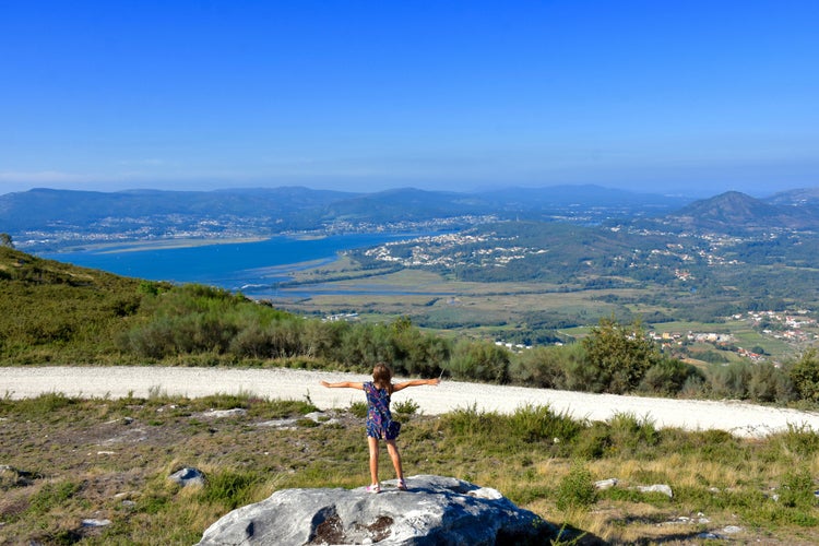 Happy young girl with her hands raised up stands on the edge of the cliff against the backdrop of a beautiful view of the sea. Viewpont. Portugal. Santo Antaо. Caminha. Viana do Castelo.