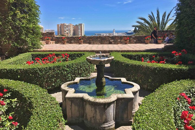 A beautiful fountain surrounded by vibrant red roses in the garden of Alcazaba showcases nature-s elegance..png