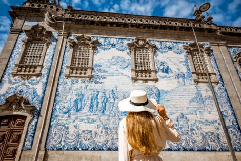 Photo of young woman tourist standing near the church with famous Portuguese blue ceramic tiles on the facade in Porto city, Portugal.