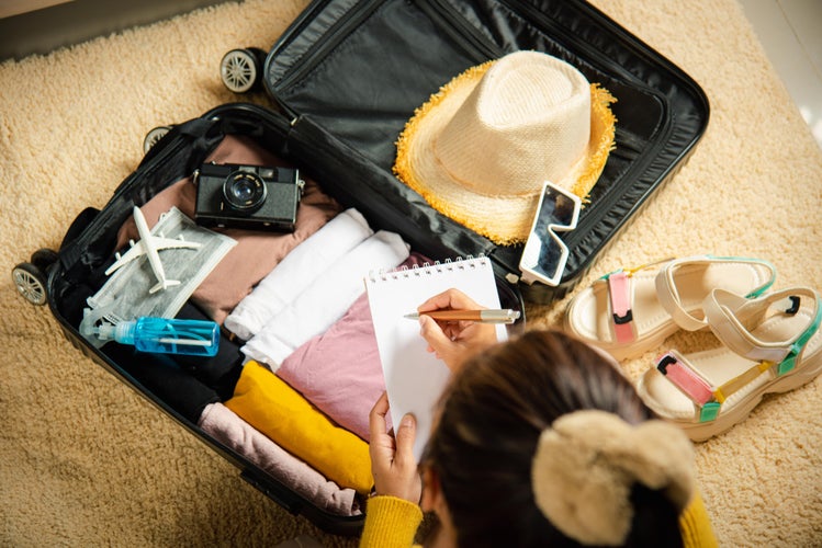 Making check list of things to pack for travel. Woman writing paper take note and packing suitcase to vacation writing paper list sitting on room, prepare clothes into luggage, Travel vacation travel in Lisbon-min.jpg