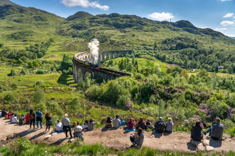 Photo of Glenfinnan Railway Viaduct seen by group of tourists in Scotland .