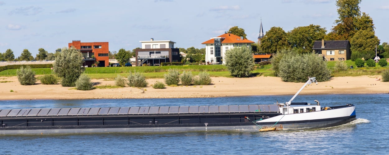 Cityscape of Nijmegen in The Netherlands with scenic view on cargo boats passing the bridge in river Waal on a sunny autumn day.