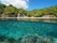 photo of Mediterranean Sea coastline with tourists in summer and a school of fish underwater, split view above and below water surface in Cala Rostella, Roses, Girona, Spain.