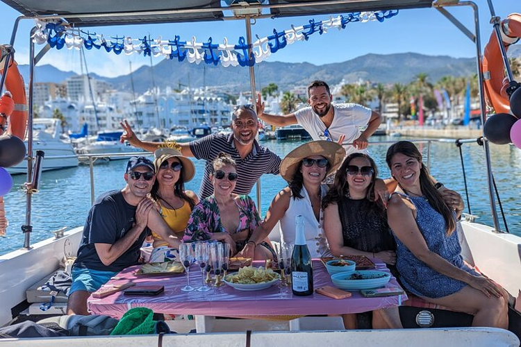 A group of people enjoying drinks and food on a boat in Benalmadena, surrounded by scenic views and a vibrant atmosphere..png