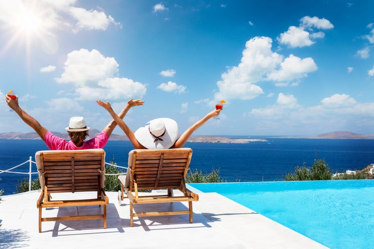 Photo of couple sitting on sunchairs enjoying the sun during their summer holidays in Mykonos.