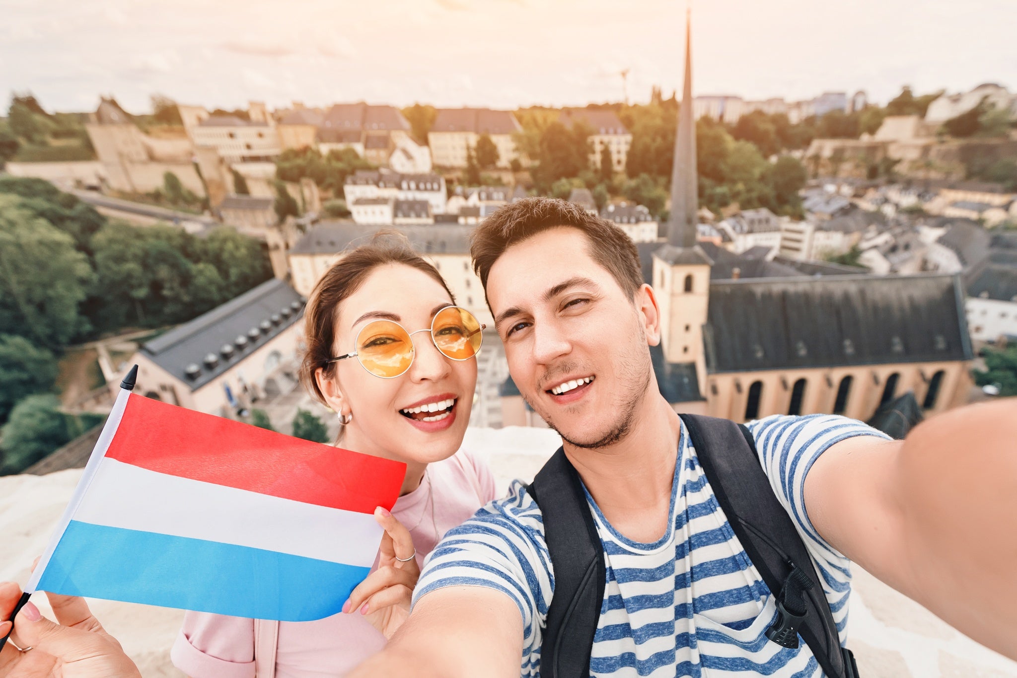 A happy couple of young people hug and take selfies with the flag of Luxembourg while sightseeing in old town.jpg