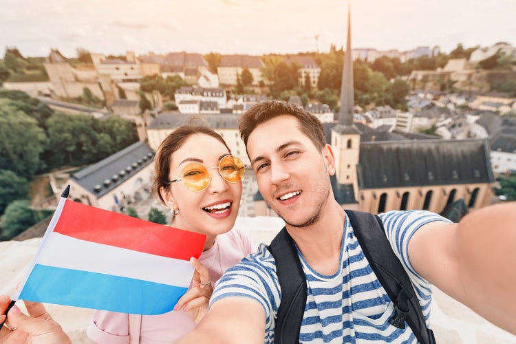 A happy couple of young people hug and take selfies with the flag of Luxembourg while sightseeing in old town.jpg