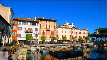 Photo of Old harbour Porto Vecchio with motor boats on turquoise water, green trees and traditional buildings in historical centre of Desenzano del Garda town, Northern Italy.