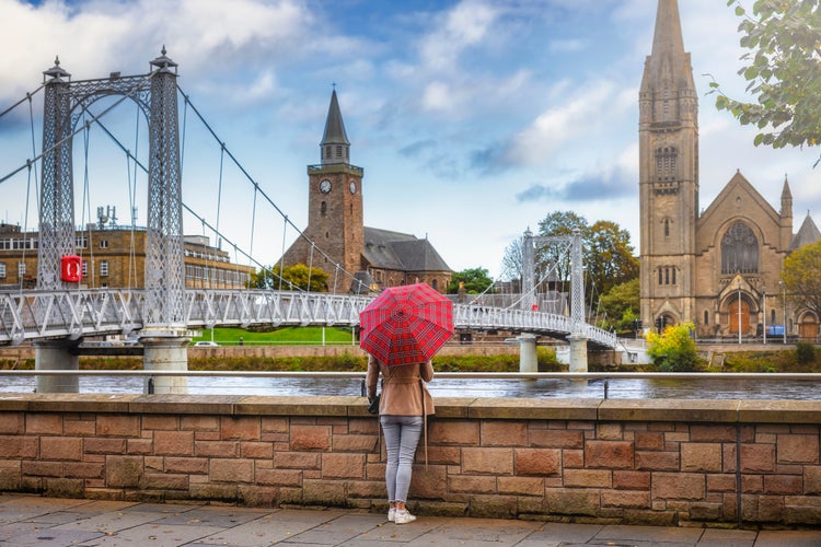 Photo of tourist woman with a scottish pattern umbrella enjoys the view to the cityscape of Inverness, Scotland, during autumn time.