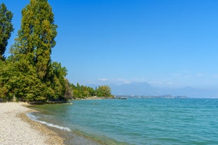 Photo of Old harbour Porto Vecchio with motor boats on turquoise water, green trees and traditional buildings in historical centre of Desenzano del Garda town, Northern Italy.