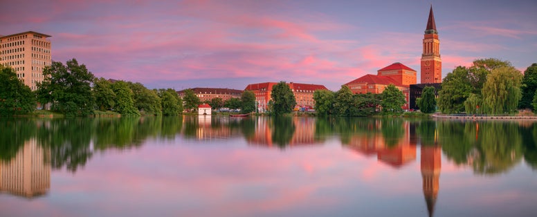 photo of view of : Kiel, Germany. Panoramic cityscape image of downtown Kiel, Germany with Town Hall, Opera House and reflection of the skyline in Small Kiel at sunset.