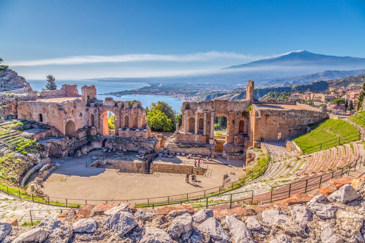 Photo of Ruins of the Ancient Greek Theater in Taormina, Sicily with the double smoke tail of the Etna extending over the the Giardini-Naxos bay of the Ionian Sea in the morning sun shine, Italy.