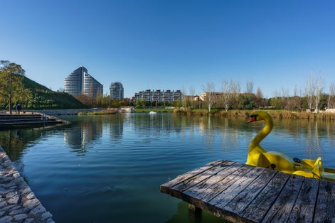 Photo of A lake inside Cabecera Park in Valencia city with buildings at background and a big yellow duck .