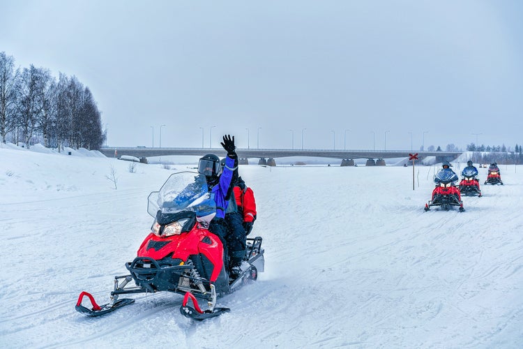 photo of people on snowmobile waving hand on the frozen lake in winter Rovaniemi, Lapland, Finland.