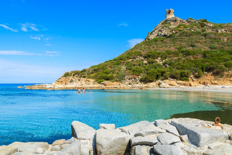 Photo of people swimming in azure sea bay near Torre de Porto Giunco tower, Sardinia island, Italy.