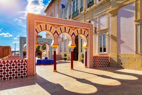View of Silves town buildings with a red and white archway and a blue fountain, Algarve region, Portugal. 