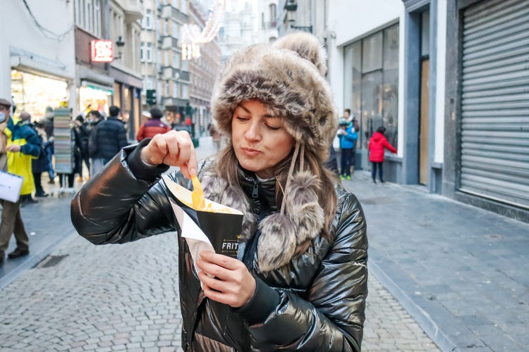 Young woman eating belgian fries on the street, people eating, traditional food, candid moments.jpg