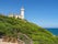 Capo Circeo Lighthouse, white tower on the slope of mountain in the blue sky background, next to the San Felice Circeo town in Italy. Beautiful Italian landscape.