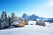 photo of winter landscape with wooden log cabin on meadow Alpe di Siusi on blue sky background on sunrise time. Dolomites, Italy. Snowy hills with orange larch and Sassolungo and Langkofel mountains group.